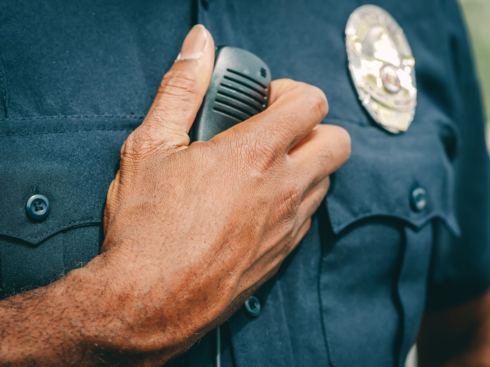 Mano de un policía sobre el radio de comunicación en su uniforme, imagen de capacitación y cooperación en seguridad