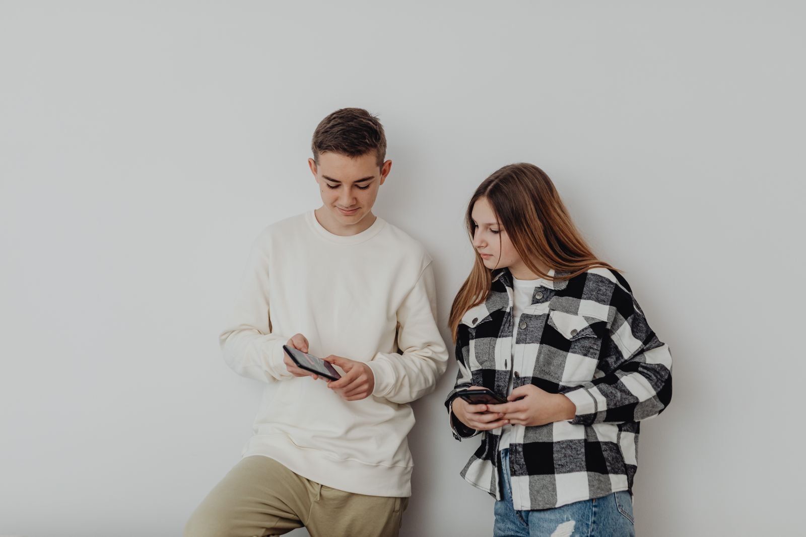 Dos adolescentes usan sus celulares junto a una pared, usuarios de redes sociales a quienes protege el decreto contra contenido violento