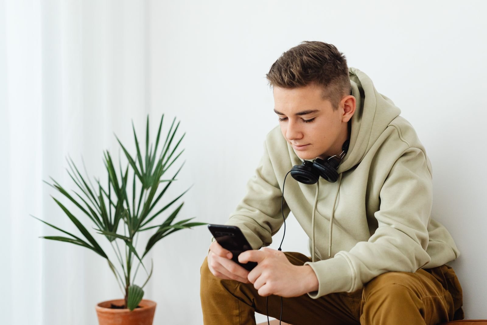 Adolescente con audífonos revisa su celular, contenido violento en redes sociales que las plataformas deberán dejar de recomendar a menores