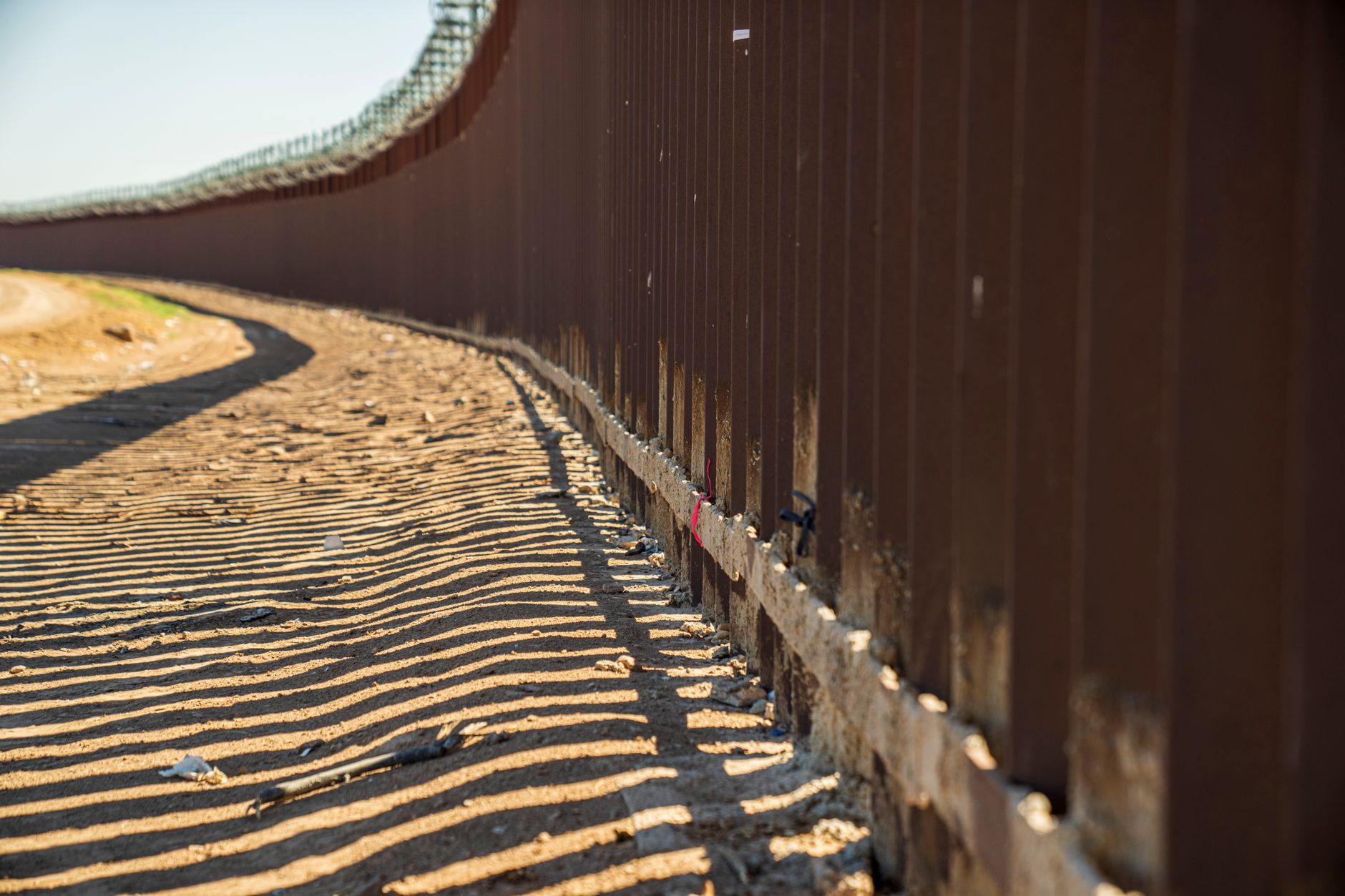 Valla metálica proyectando sombras sobre la arena, imagen de referencia de la frontera donde rige la restricción de drones