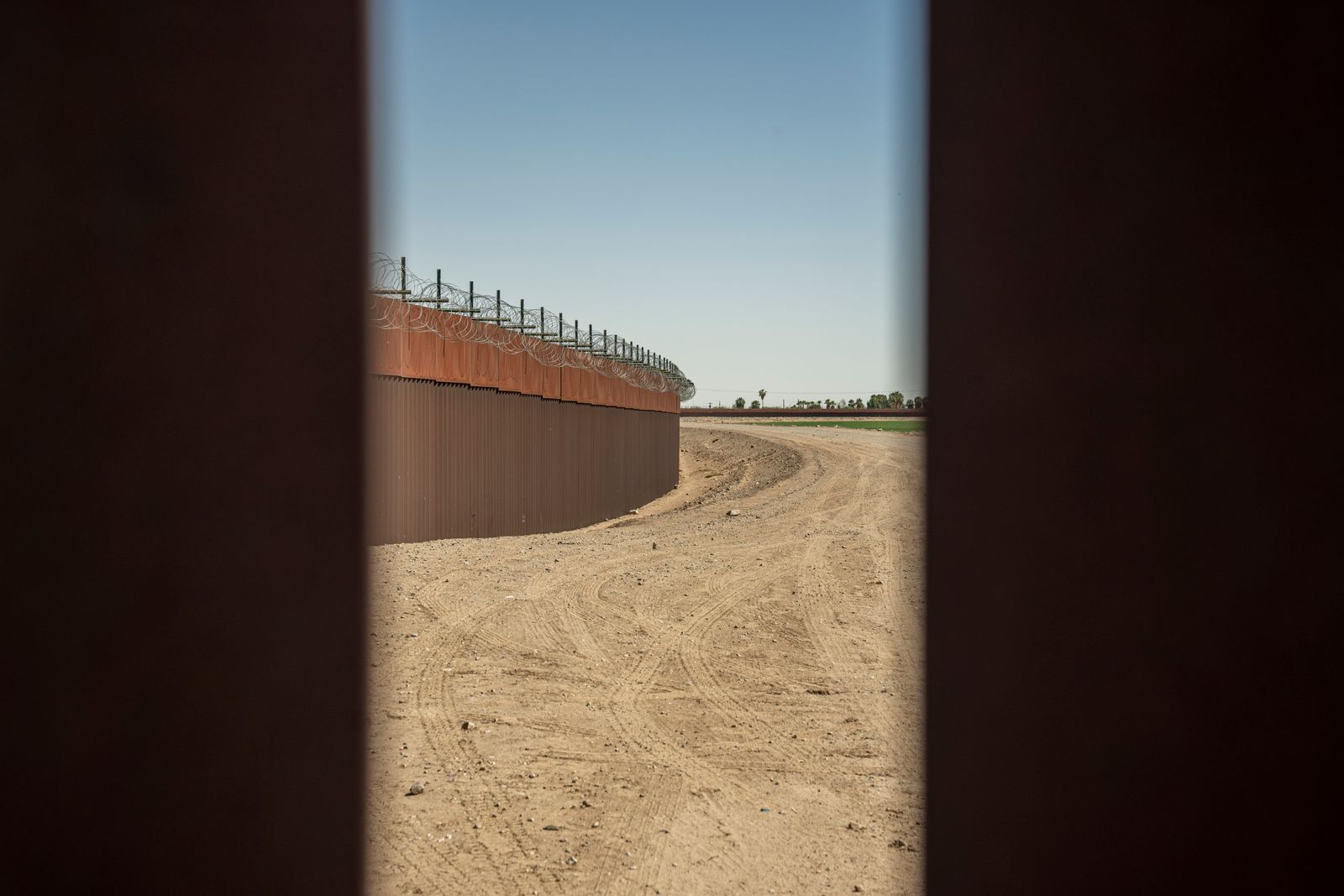 Muro fronterizo con alambre de púas junto a un camino de tierra, frontera entre México y Estados Unidos